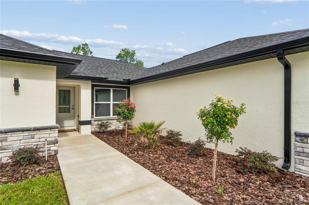 A concrete walkway leads to the front entrance of a house with light-colored stucco walls — 15093 GONZO ROAD, WEEKI WACHEE, FL
