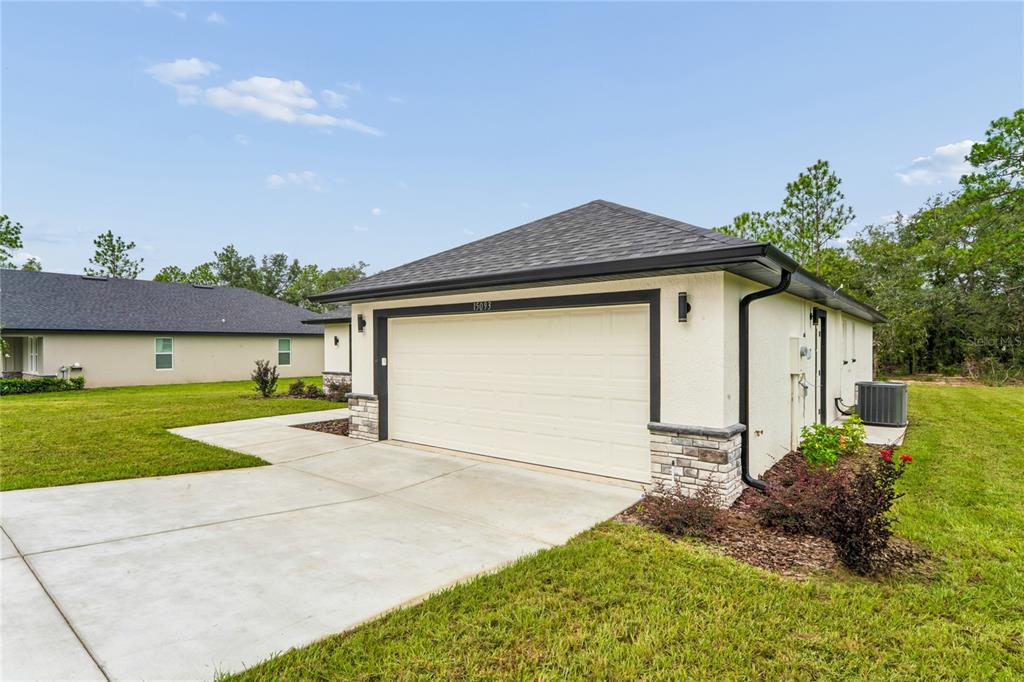 A beige house exterior features a two-car garage, stone accents, and a concrete driveway — 15093 GONZO ROAD, WEEKI WACHEE, FL