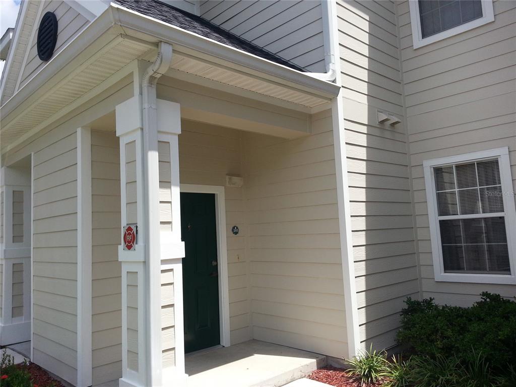 The exterior view shows a covered entryway with a green door and beige siding — 200 SOUTHERN PECAN CIRCLE UNIT 203, WINTER GARDEN, FL