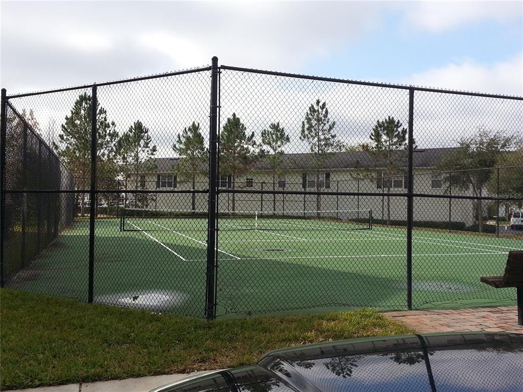 A fenced-in outdoor tennis court with a green surface sits in front of a building — 200 SOUTHERN PECAN CIRCLE UNIT 203, WINTER GARDEN, FL