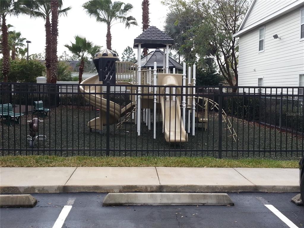 A fenced playground with slides and a climbing structure sits next to a white building — 200 SOUTHERN PECAN CIRCLE UNIT 203, WINTER GARDEN, FL