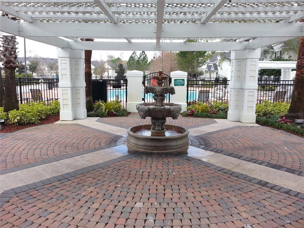 A tiered stone fountain sits in the center of a brick patio under a pergola — 200 SOUTHERN PECAN CIRCLE UNIT 203, WINTER GARDEN, FL