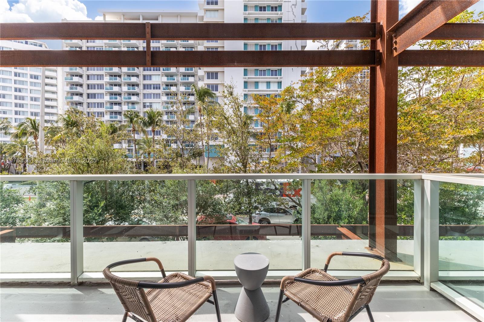 A balcony features two wicker chairs, a small side table, and a glass railing — 1215 West Ave # 203, Miami Beach FL 33139, MIAMI BEACH, FL