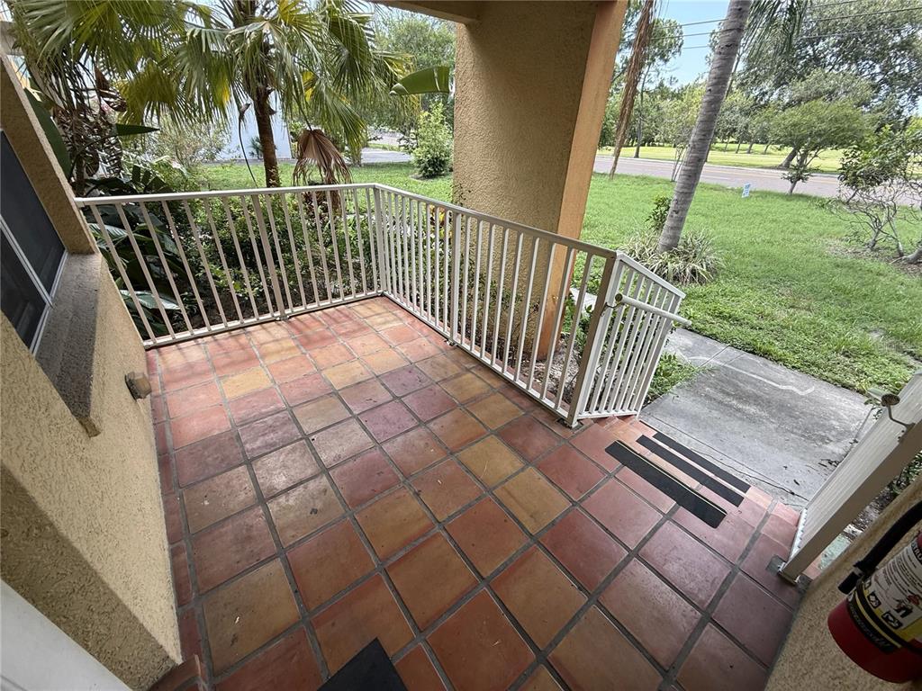 A tiled outdoor patio features a white metal railing and steps leading to a lawn — 1355 DREW STREET UNIT 101, CLEARWATER, FL