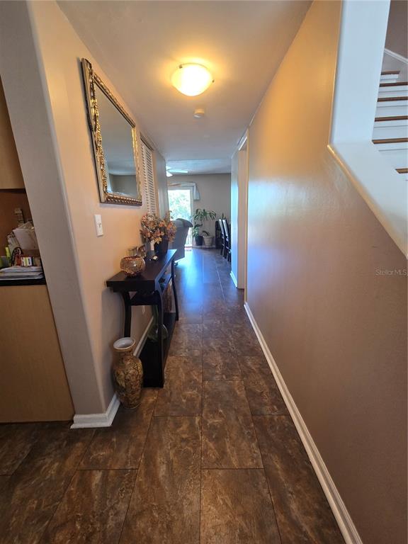 A hallway with brown tile flooring leads toward a living area with a sliding door — 6305 NEWTOWN CIRCLE UNIT 5B4, TAMPA, FL