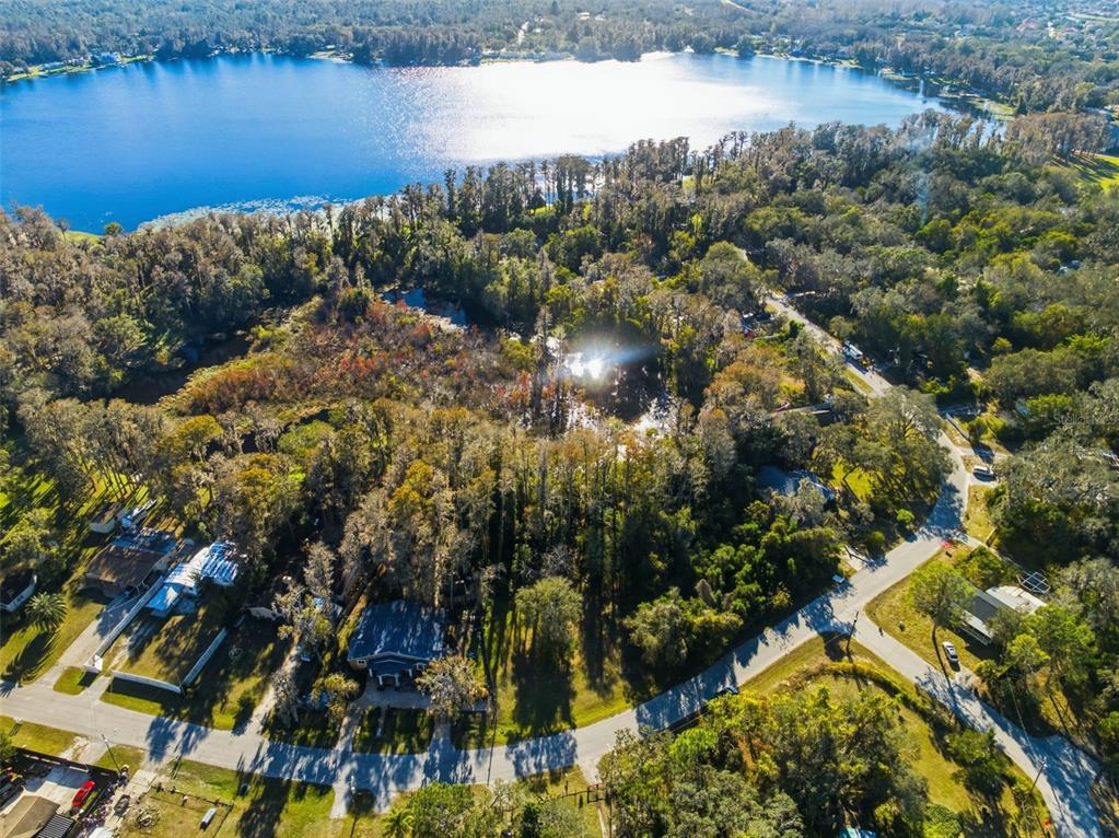 An aerial view shows a house surrounded by dense trees near a large lake — 0 MOON LAKE CIRCLE, NEW PORT RICHEY, FL