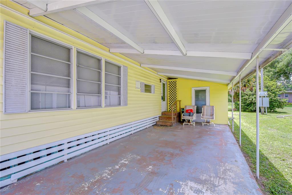 A covered concrete patio sits beside a yellow mobile home with two outdoor chairs — 37344 HAMMOND DRIVE, ZEPHYRHILLS, FL
