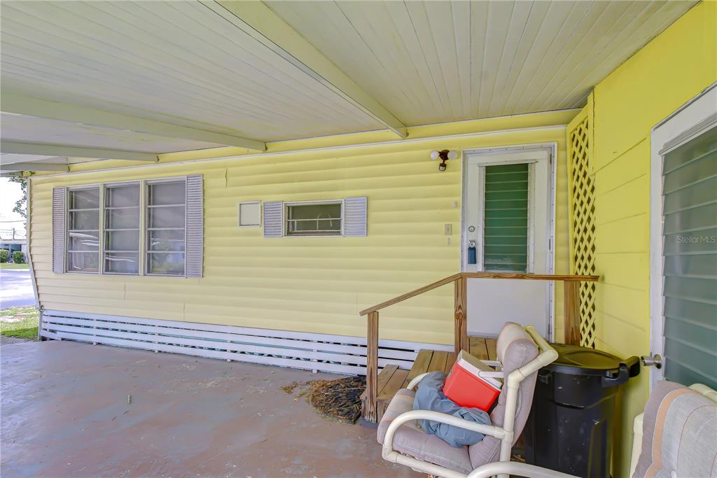 A yellow mobile home exterior features a covered concrete patio, a wooden railing, and windows — 37344 HAMMOND DRIVE, ZEPHYRHILLS, FL