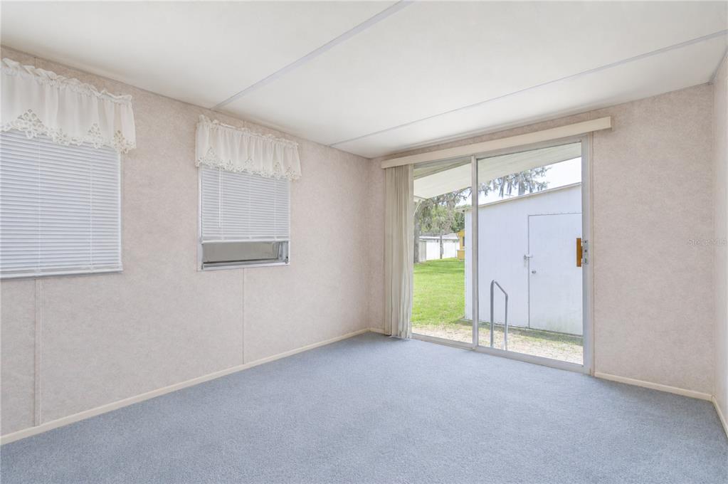An empty room with light-colored walls, blue carpeting, two windows, and a sliding glass door — 37344 HAMMOND DRIVE, ZEPHYRHILLS, FL