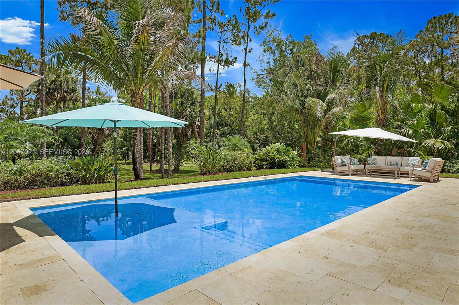 A rectangular swimming pool with a light blue umbrella sits on a stone patio — 12127 N 154th Rd N, Jupiter FL 33478, JUPITER, FL