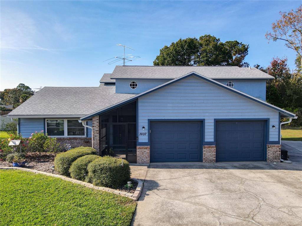 A two-story blue house features a two-car garage, a screened entryway, and a front lawn — 1807 VIRGINIA COURT, TAVARES, FL