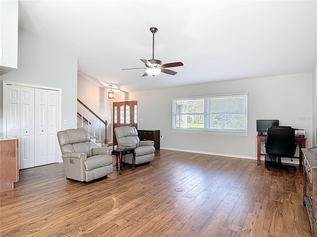 A living room features wood-look flooring, two gray recliners, a desk, and a staircase — 1807 VIRGINIA COURT, TAVARES, FL