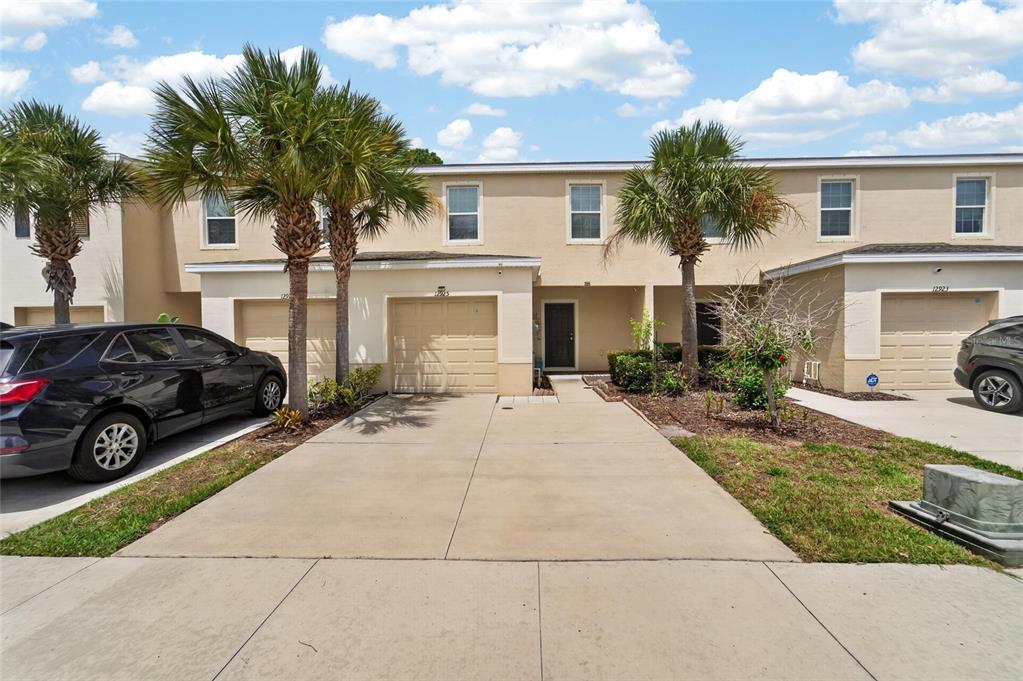 A two-story townhouse exterior with a concrete driveway, attached garage, and palm trees — 12925 SHADY FERN LANE, GIBSONTON, FL