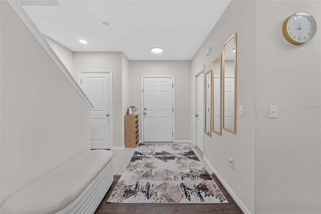 A bright entryway features a white door, a patterned rug, and three gold-framed wall mirrors — 12925 SHADY FERN LANE, GIBSONTON, FL