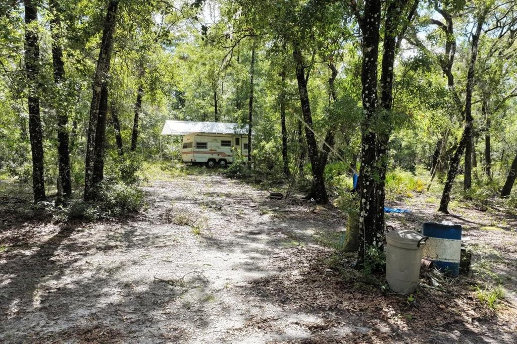 A vintage camper sits on a wooded lot with a metal roof cover — 0000 SW COUNTY ROAD 347, CHIEFLAND, FL
