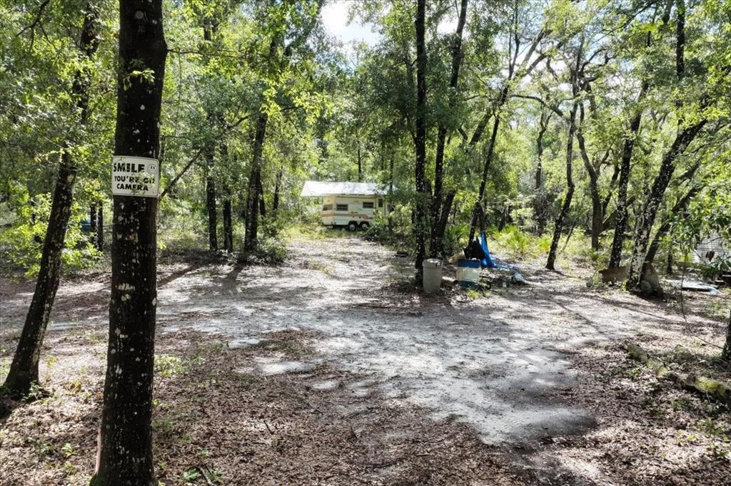 A vintage camper sits in a wooded clearing with a security sign on a tree — 0000 SW COUNTY ROAD 347, CHIEFLAND, FL