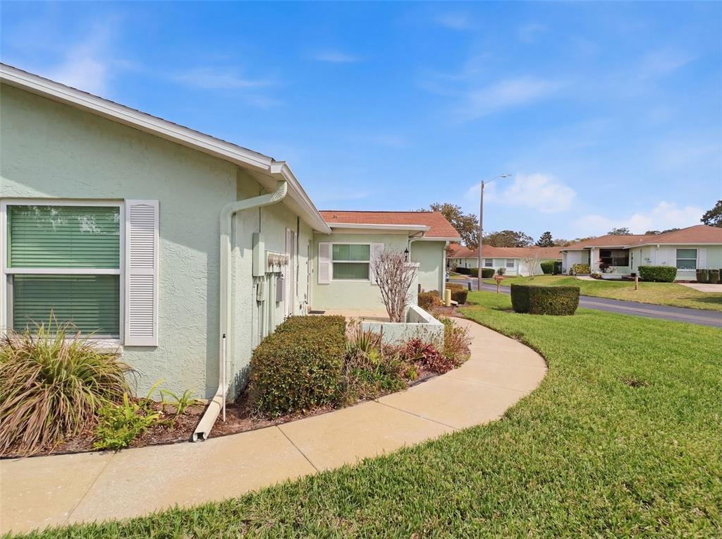 A light green single-story house exterior features a concrete walkway and a small landscaped garden — 11341 DOLLAR LAKE DRIVE UNIT 1, PORT RICHEY, FL