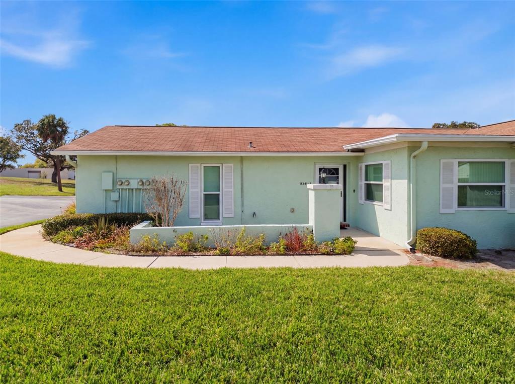A light green single-story house features a brown shingled roof and a front garden bed — 11341 DOLLAR LAKE DRIVE UNIT 1, PORT RICHEY, FL