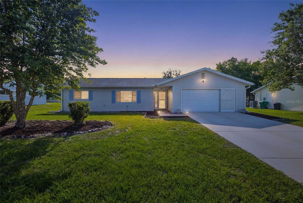 A single-story house with light siding, blue shutters, and a concrete driveway at dusk — 11089 SW 78TH COURT, OCALA, FL