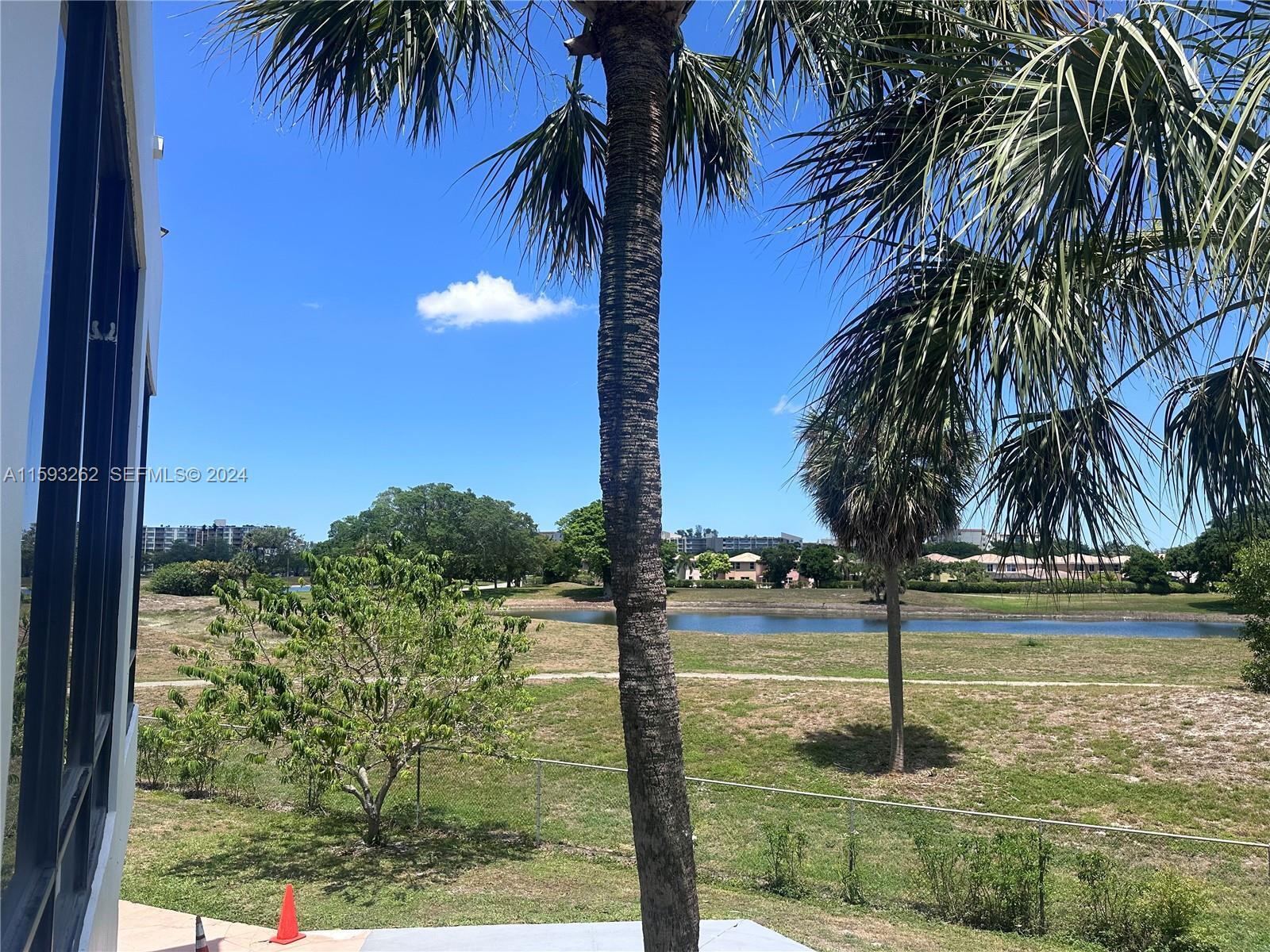 A view of a grassy field, a small pond, and palm trees from a balcony — 7021 Environ Boulevard # 317, Lauderhill FL 33319, LAUDERHILL, FL