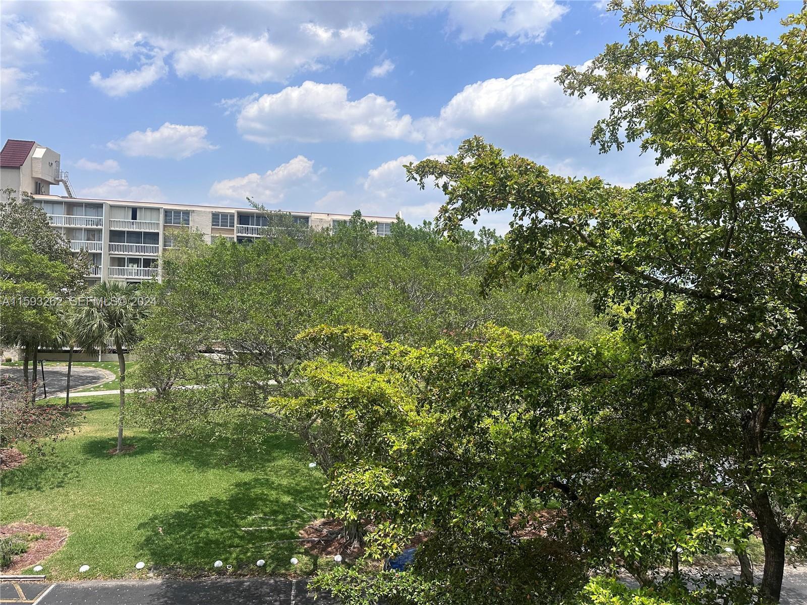 A view of a grassy courtyard and trees in front of a multi-story apartment building — 7021 Environ Boulevard # 317, Lauderhill FL 33319, LAUDERHILL, FL