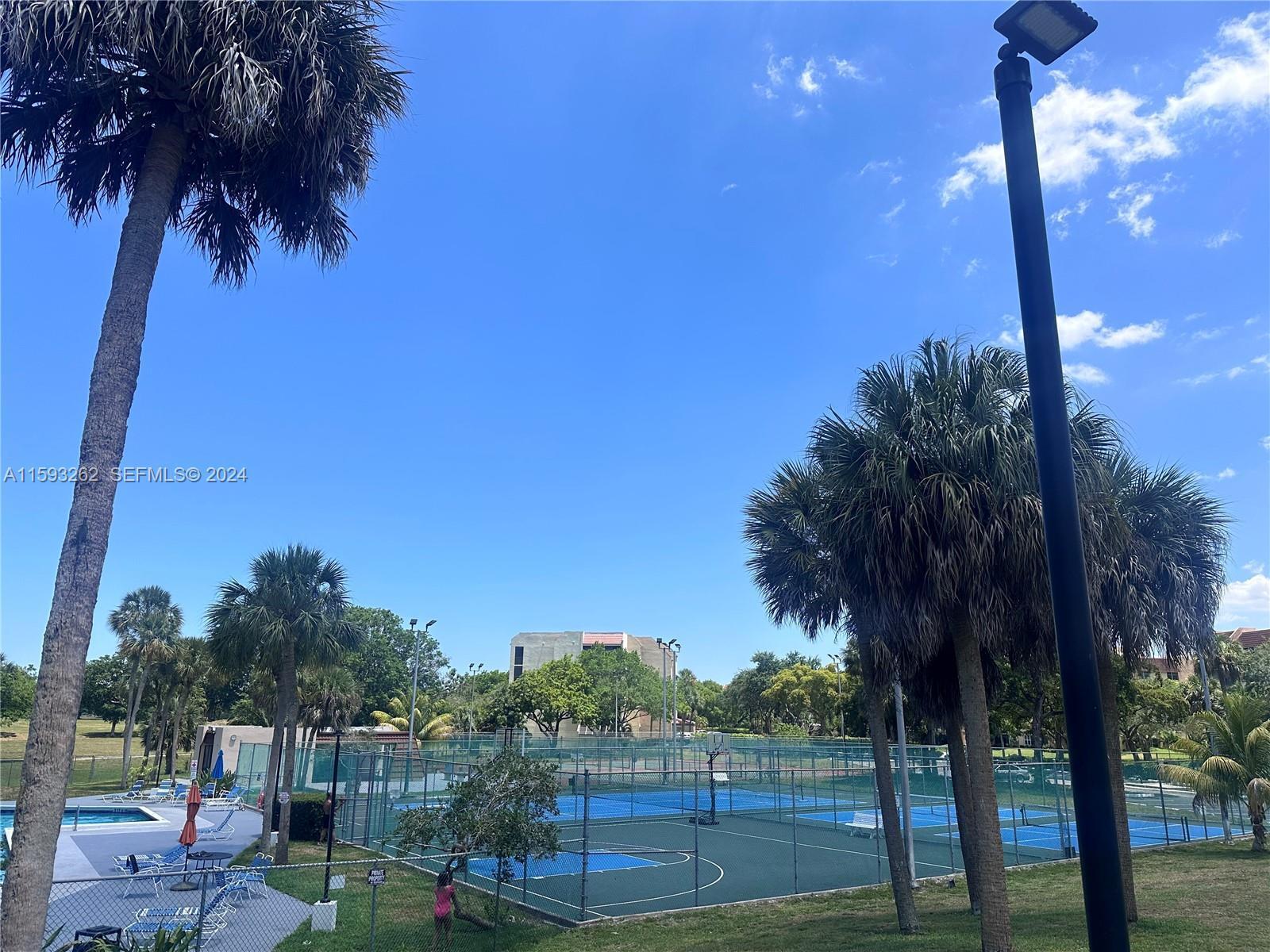 A fenced tennis court sits outdoors surrounded by palm trees under a blue sky — 7021 Environ Boulevard # 317, Lauderhill FL 33319, LAUDERHILL, FL