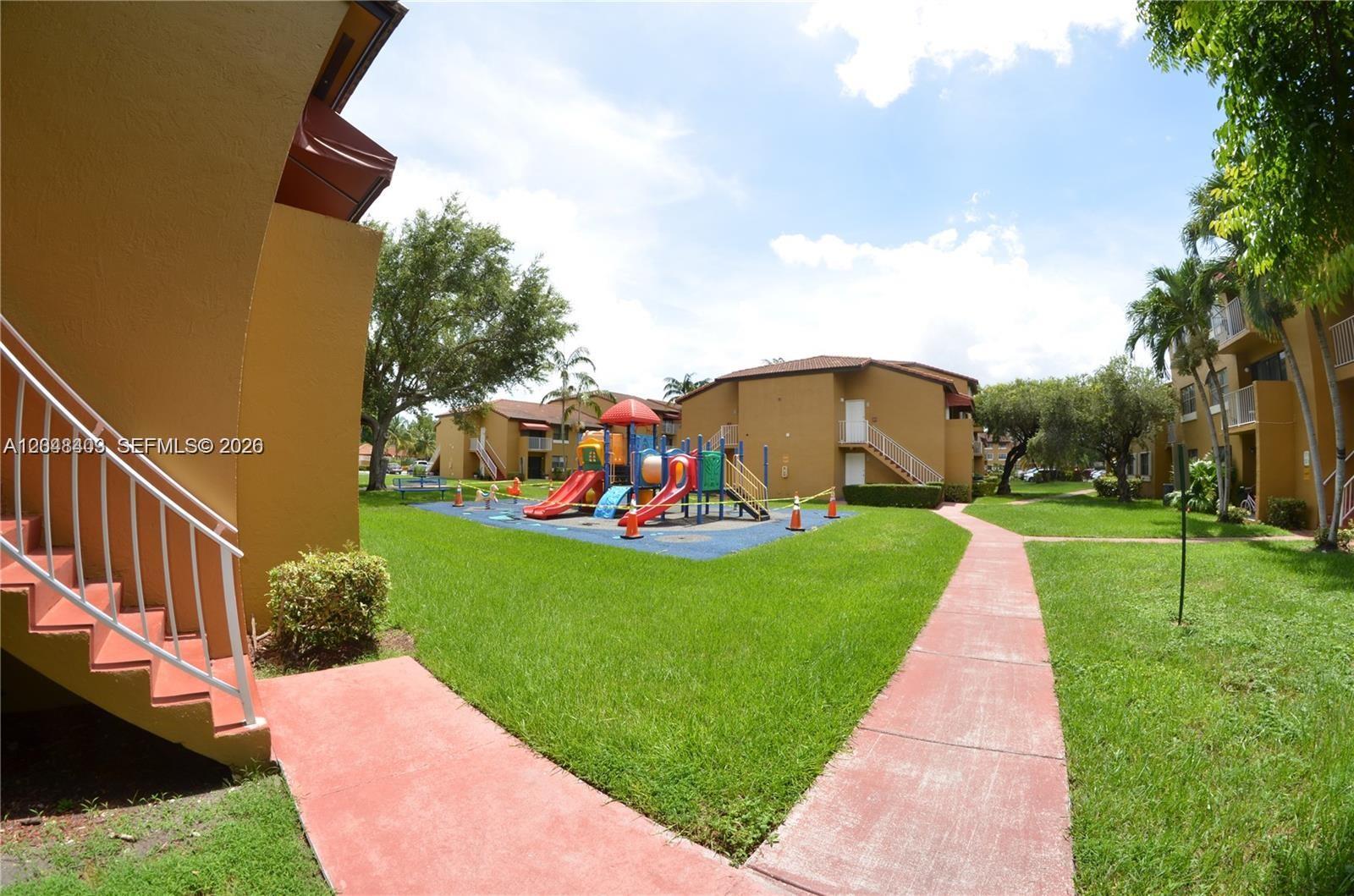 A playground with slides sits on a grassy lawn between apartment buildings — 15630 SW 80th St # 210, Miami FL 33193, MIAMI, FL