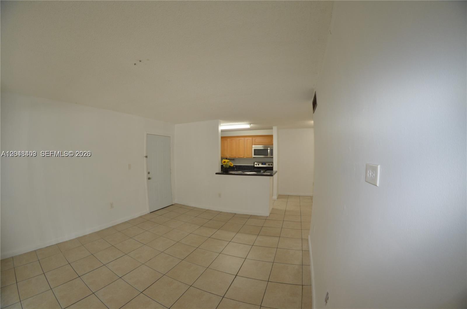 An open living area with tile flooring leads to a kitchen with wood cabinets — 15630 SW 80th St # 210, Miami FL 33193, MIAMI, FL