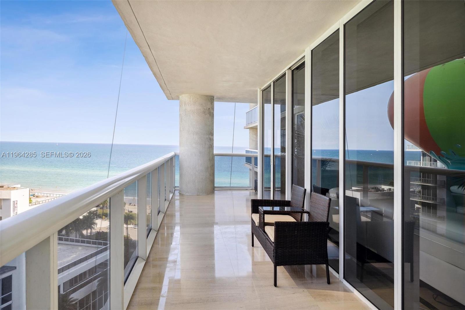 A balcony with a glass railing, tiled floor, and two chairs overlooks the ocean — 1800 S Ocean Dr # 1010, Hallandale Beach FL 33009, HALLANDALE BEACH, FL