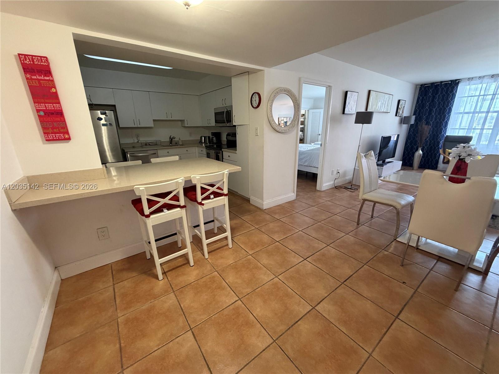 A kitchen with white cabinets and a breakfast bar opens into a tiled dining area — 5161 Collins Ave # 310, Miami Beach FL 33140, MIAMI BEACH, FL