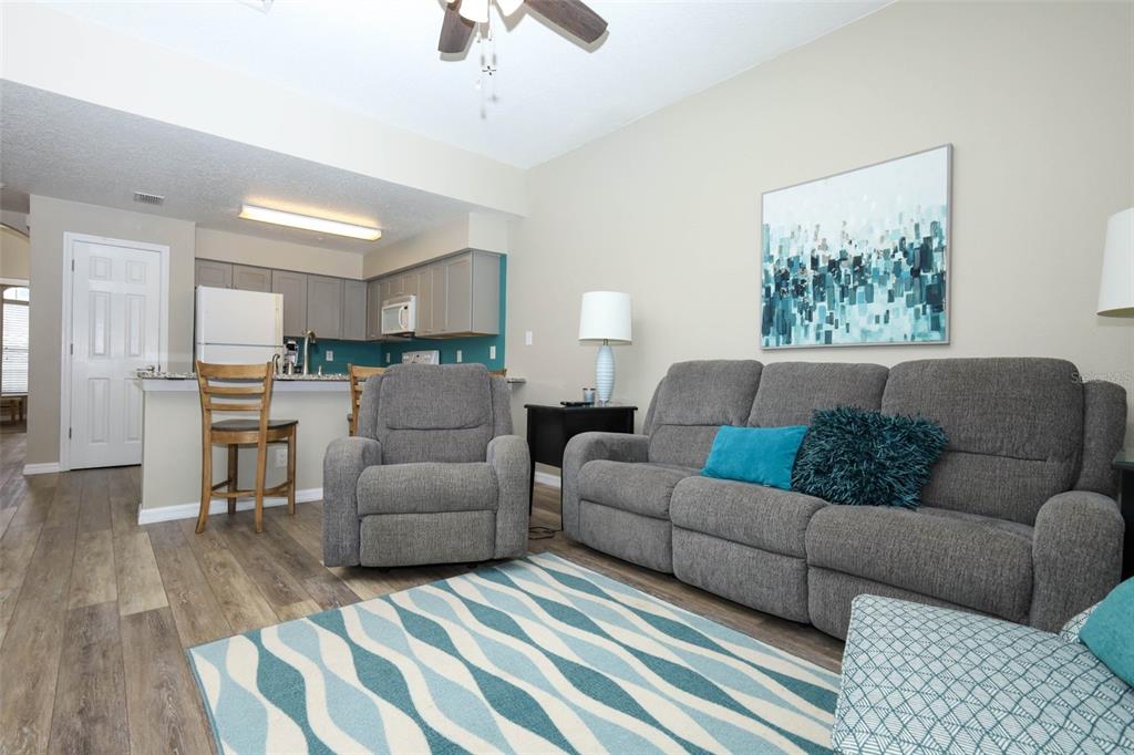 A living room with a grey sofa, recliner, patterned rug, and an open kitchen area — 694 SEABROOK COURT UNIT 101, ALTAMONTE SPRINGS, FL