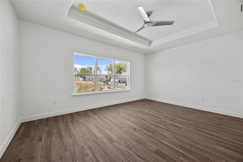 An empty bedroom features white walls, wood-look tile flooring, a tray ceiling, and a window — 1132 SW 67TH WAY, GAINESVILLE, FL