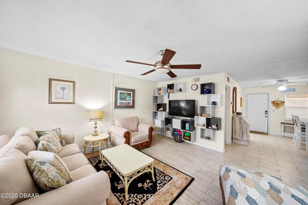 A living room features a beige sofa, an armchair, a television, and light-colored tile flooring — 3750 S ATLANTIC AVENUE UNIT 190, DAYTONA BEACH, FL