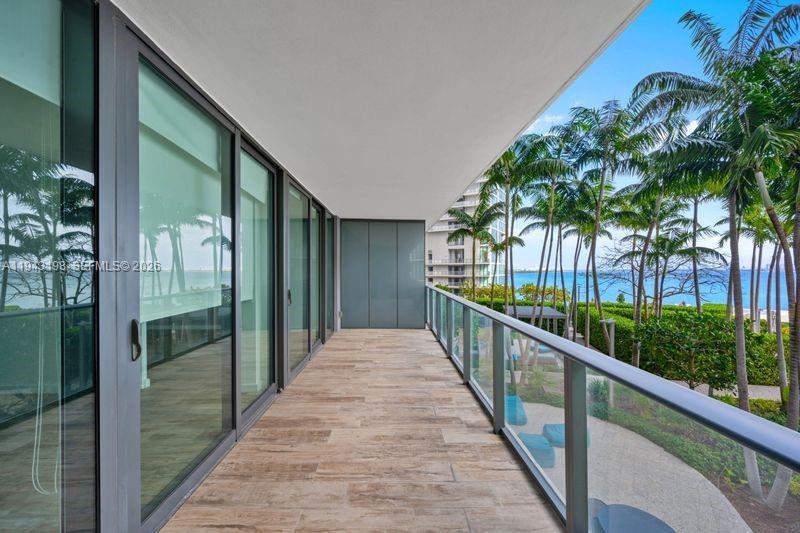 A balcony with wood-look tile flooring, glass railings, and views of palm trees and water — 650 NE 32nd St # 602, Miami FL 33137, MIAMI, FL