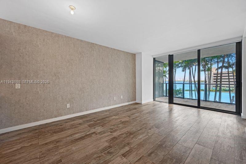 An empty room features wood-look tile flooring, a textured accent wall, and floor-to-ceiling balcony windows — 650 NE 32nd St # 602, Miami FL 33137, MIAMI, FL