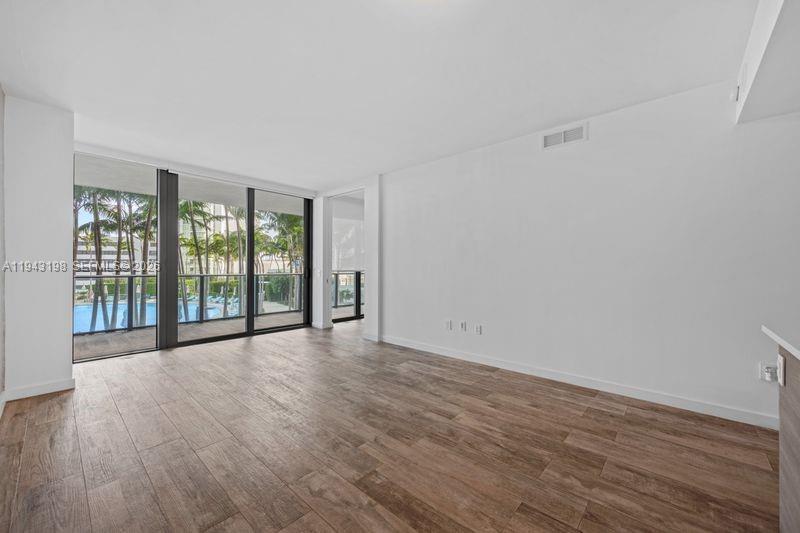 An empty living room with wood-look tile flooring and floor-to-ceiling windows overlooking a pool — 650 NE 32nd St # 602, Miami FL 33137, MIAMI, FL