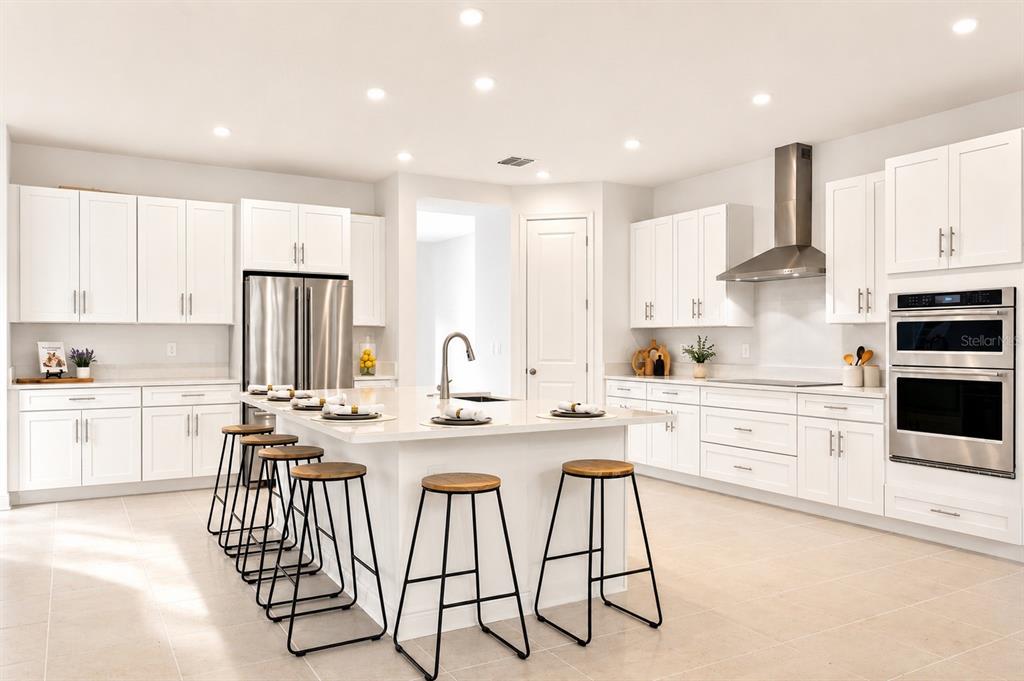 A modern white kitchen features a large center island with bar stools and stainless appliances — 4614 W EUCLID AVENUE, TAMPA, FL