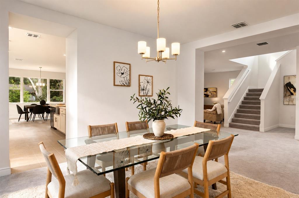 A dining room with a glass table, light wood chairs, and a chandelier near stairs — 4614 W EUCLID AVENUE, TAMPA, FL