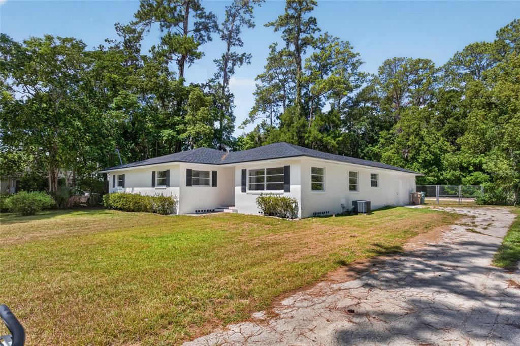A white, single-story house with a dark roof sits on a grassy lot with trees — 1220 NE 16TH AVENUE, OCALA, FL