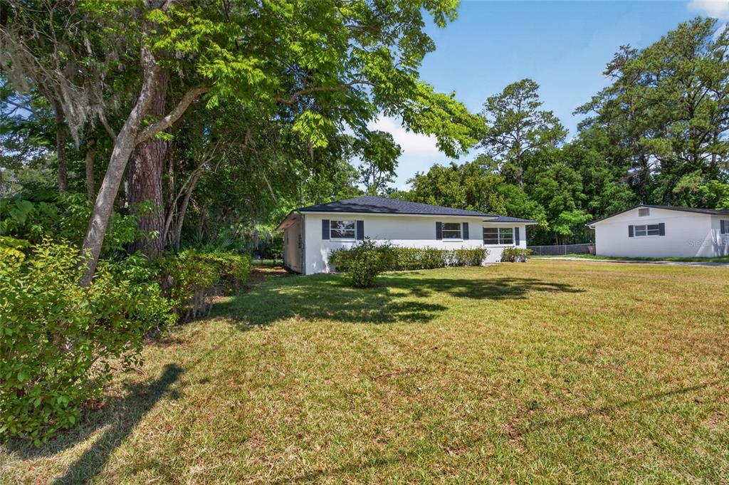 A white single-story house with a dark roof sits on a grassy lot with trees — 1220 NE 16TH AVENUE, OCALA, FL