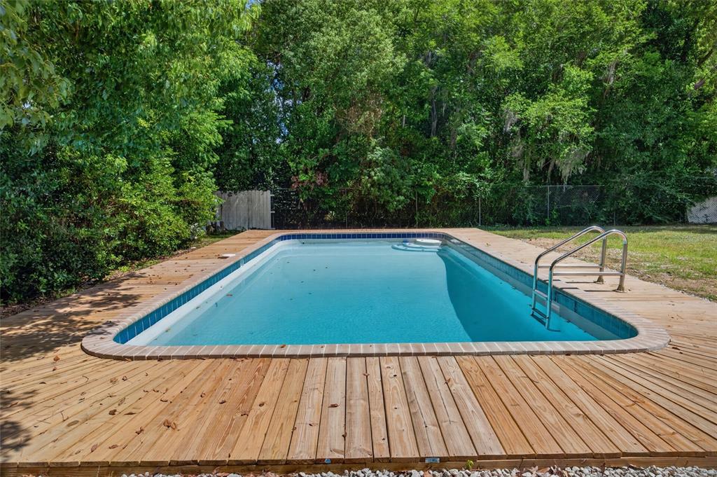 An outdoor rectangular swimming pool is surrounded by a wooden deck and dense green trees — 1220 NE 16TH AVENUE, OCALA, FL