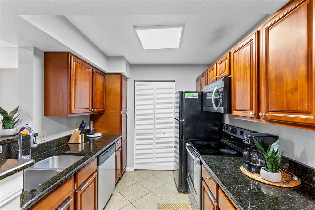 A galley-style kitchen features wood cabinets, dark granite countertops, and black appliances — 1021 S HIAWASSEE ROAD UNIT 3928, ORLANDO, FL