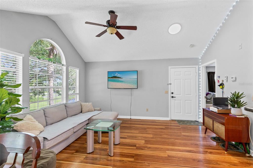 A living room with a vaulted ceiling, hardwood floors, a sectional sofa, and a television — 1021 S HIAWASSEE ROAD UNIT 3928, ORLANDO, FL