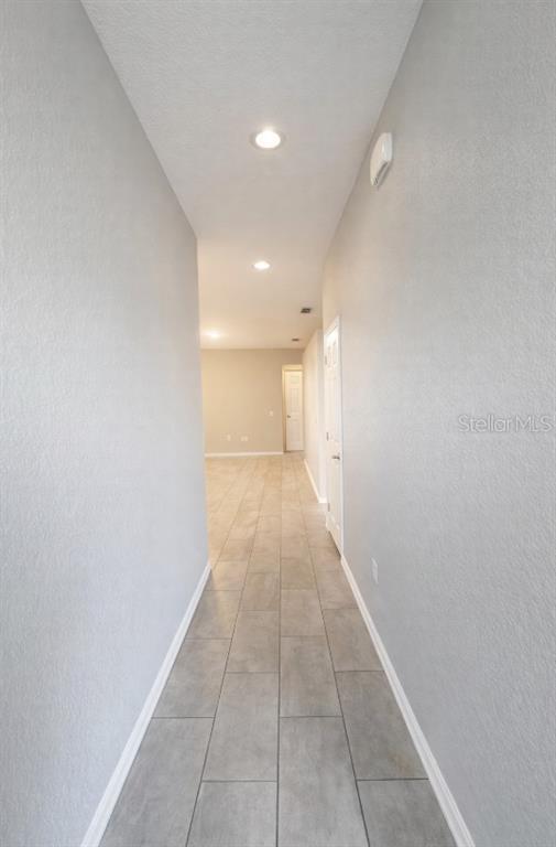 A hallway with light gray walls and rectangular gray tile flooring leads to an open room — 1192 NORMANDY, WINTER HAVEN, FL