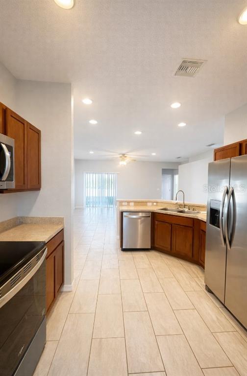 A kitchen with wood cabinets, stainless steel appliances, and tile flooring opens to a living area — 1192 NORMANDY, WINTER HAVEN, FL