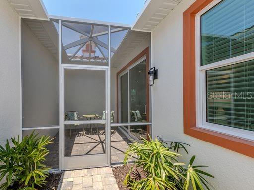 A screened-in patio with a paver floor, small table, and chairs sits beside a house — 124 CLIFTON WAY, VENICE, FL