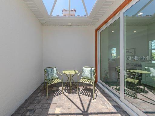 A small outdoor patio with a paver floor, two chairs, a table, and a skylight — 124 CLIFTON WAY, VENICE, FL