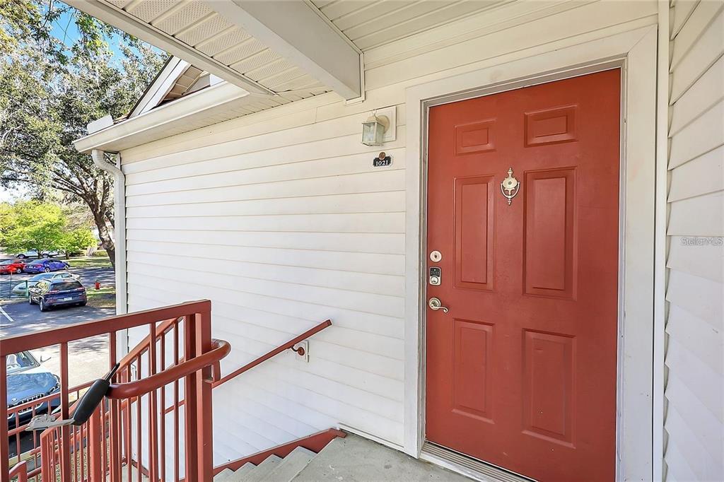 An exterior view of a red front door with a metal railing and stairs — 11568 WESTWOOD BOULEVARD UNIT 1021, ORLANDO, FL