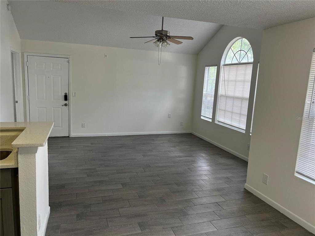 An empty living room features vaulted ceilings, a ceiling fan, and gray wood-look tile flooring — 11568 WESTWOOD BOULEVARD UNIT 1021, ORLANDO, FL