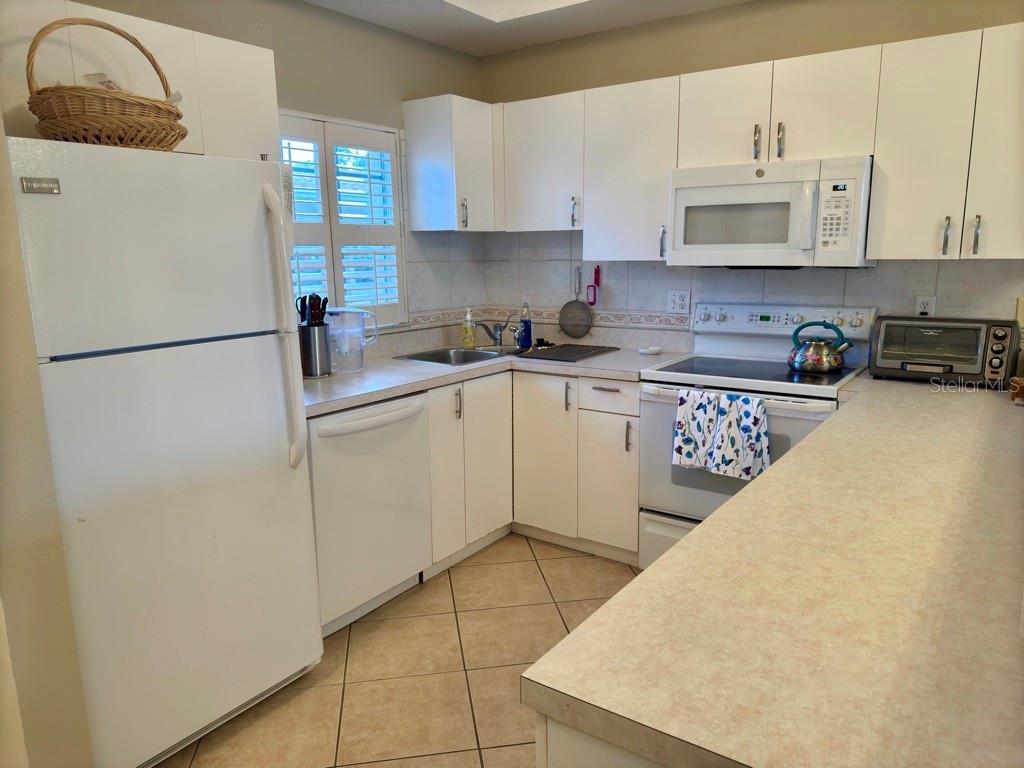 A kitchen features white cabinets, white appliances, a tiled floor, and a laminate countertop — 8370 WINGATE DRIVE UNIT 714, SARASOTA, FL